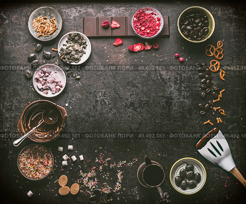Homemade chocolate factory background. Various chocolate topping , melted chocolate in bowls , spatula, nuts, marshmallow, nuts, liquorice, caramel and candy on dark table. Top view. Copy space. Стоковое фото, агентство Ingram Publishing / Фотобанк Лори