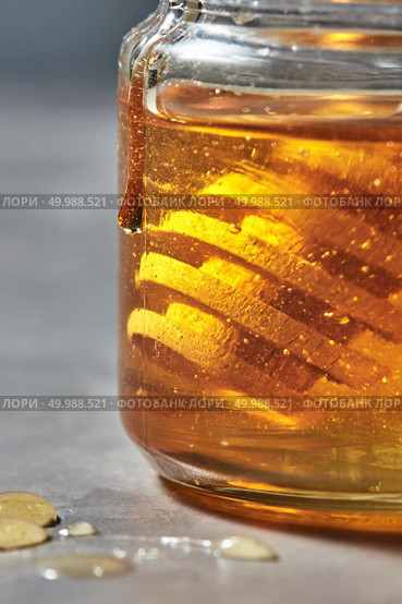 Honey background with natural flower yellow honey in glass pot with wooden dipper, traditional pure natural sweet goodness.. Close-up view of glass jar with golden honey and wooden dipper on a gray background. Jewish New Year healthy holiday . Стоковое фото, агентство Ingram Publishing / Фотобанк Лори