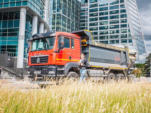 HOWO dump truck parked against the backdrop of modern glass office buildings in the city. Редакционное фото, фотограф Константин Григорьев / Фотобанк Лори
