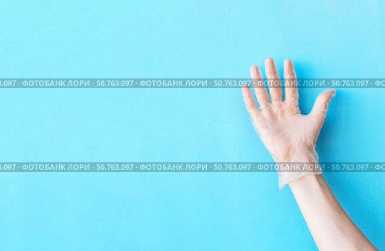 Human hand in transparent vinyl glove raised above light blue background. Safety and selfcare concept. Стоковое фото, фотограф Акимова Надежда / Фотобанк Лори