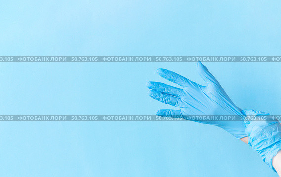 Human hands puting on blue nitrile disposable glove above light blue background. Safety first concept. Стоковое фото, фотограф Акимова Надежда / Фотобанк Лори