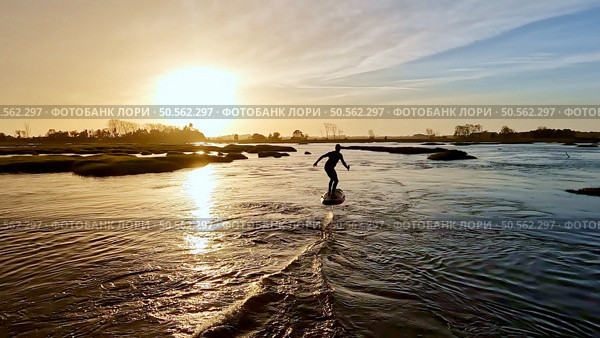 Hydrofoil rider gliding over the water with his board in one of the canals of the Ria de Aveiro in Portugal during sunset. Стоковое фото, агентство Ingram Publishing / Фотобанк Лори