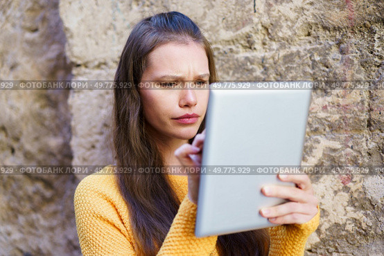 In a beautiful outdoor setting, a young woman in a colorful sweater focuses on her tablet, showcasing the balance between modern tech and concentration, reflecting her dedication to learning. A Young Woman Engaged in Using a Tablet Outdoors, Displaying Strong Focus and Intention. Стоковое фото, агентство Ingram Publishing / Фотобанк Лори