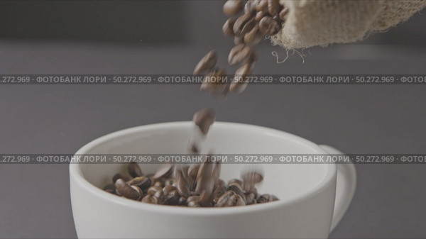 In a white cup, pour the roasted coffee beans from the bag around a dark background. Slow motion, Full HD video, 240fps, 1080p.. Roasted coffee beans poured from the bag, in a cup around a dark background. Стоковое фото, агентство Ingram Publishing / Фотобанк Лори