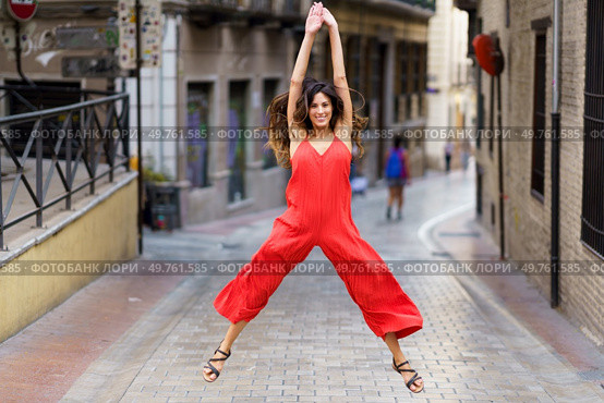 In an urban alley, a woman in a striking red jumpsuit catches attention with her energetic dance, showcasing her joyful spirit and inviting onlookers to share in her vibrant enthusiasm. A Joyful Dance Pose Captured in an Urban Alley An Exciting and Vibrant Fashion Scene. Стоковое фото, агентство Ingram Publishing / Фотобанк Лори