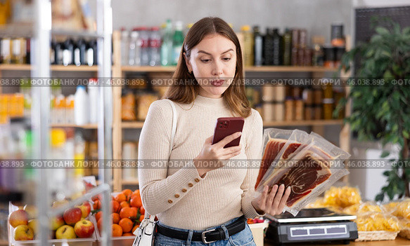 In trading floor of minimarket, girl buyer inspects hamon, scan QR code on product label. Стоковое фото, фотограф Яков Филимонов / Фотобанк Лори