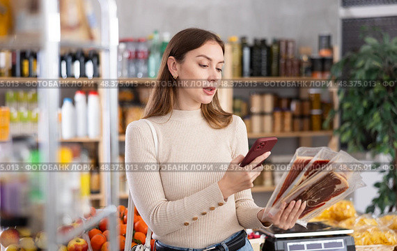 In trading floor of minimarket, girl buyer inspects hamon, scan QR code on product label. Стоковое фото, фотограф Яков Филимонов / Фотобанк Лори