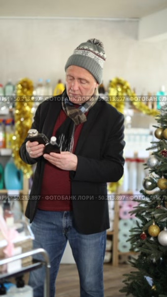 In X mas atmosphere, senior man sniffs fragrance of perfume, chooses scent spray with pleasant smell. Стоковое видео, видеограф Яков Филимонов / Фотобанк Лори