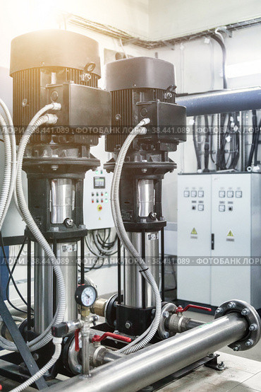 Industrial pumps in an engine room. Industry interior of water pump, valves, pressure gauges, motors inside technical room. Urban modern powerful pipelines. Automatic control systems. Copy text space. Стоковое фото, фотограф Aleksandr Golubev / Фотобанк Лори