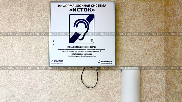 Информационная система "Исток". Знак системы слуховой петли, установленный на стене, указывающий на зону, оборудованную для слуховых аппаратов. Предоставляет четкие инструкции для пользователей, которым требуется улучшенная слуховая помощь. Редакционное фото, фотограф Анастасия / Фотобанк Лори