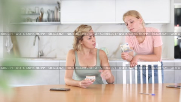 Interested teenage girl asking for pocket money from mother sitting at table in kitchen, counting received salary. Стоковое видео, видеограф Яков Филимонов / Фотобанк Лори