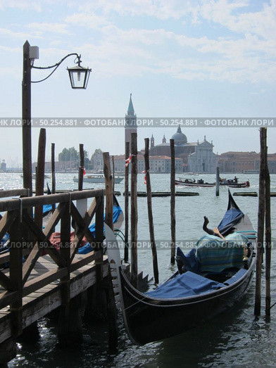 Italian traditional gondola parking near old wooden berth on the background of view of San Giorgio Maggior Church Venice, Italy.. Old wooden pier with parking italian tradition gondola. Стоковое фото, агентство Ingram Publishing / Фотобанк Лори