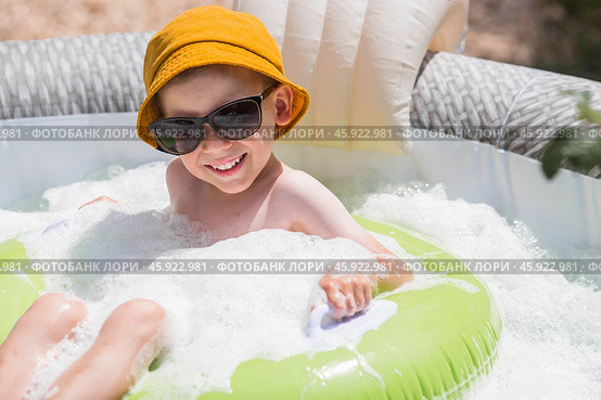 It's a hot day. A cute boy in sunglasses and a panama hat swims on a circle in a foam pool. The concept of summer holidays with children. Стоковое фото, фотограф Photojuli / Фотобанк Лори