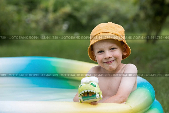 It's a hot day. A cute boy is swimming and splashing in the pool. A happy little boy smiles at the camera. Splashes of water are flying in all directions. The concept of summer holidays with children. Стоковое фото, фотограф Photojuli / Фотобанк Лори