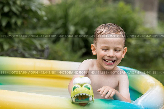 It's a hot day. A cute boy is swimming and splashing in the pool. A happy little boy smiles at the camera. Splashes of water are flying in all directions. The concept of summer holidays with children. Стоковое фото, фотограф Photojuli / Фотобанк Лори