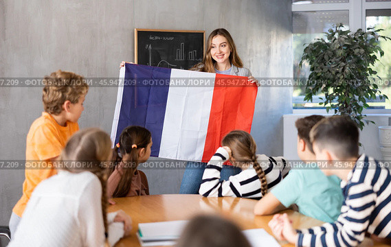 Joyful female teacher discussing with preteens students state flag of France in auditory of middle school. Стоковое фото, фотограф Яков Филимонов / Фотобанк Лори