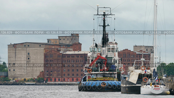 Kaliningrad, Russia - June 20, 2022: Industrial part of the city. Bank of Pregol River. Different ships. Tug boat in seaport on the Pregolya River. Редакционное фото, фотограф YuryKara / Фотобанк Лори