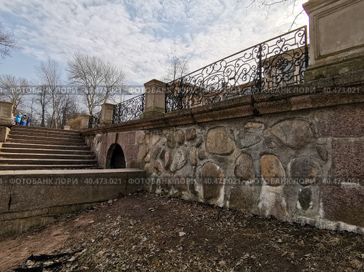 Каменный спуск к воде и красивая ограда у Дачи Громова ,  в Лопухинском саду, который расположен в конце Каменностровского проспекта на Аптекарском острове в Санкт-Петербурге. Ранняя весна, деревья, кованая решетка и лестница на  фоне красивого голубого неба с облаками. (2021 год). Стоковое фото, фотограф Елена Яворская / Фотобанк Лори
