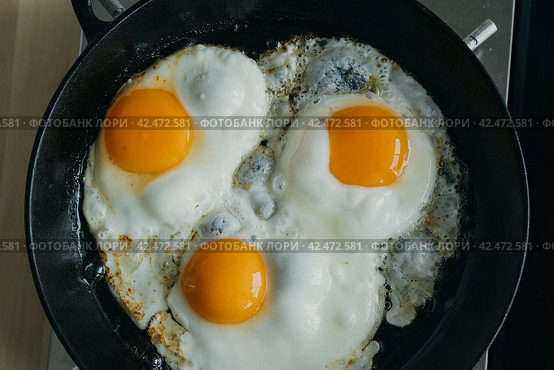 Keto meal eggs frying on hot cast iron frying pan, three fried yellow yolk, ketogenic diet. Стоковое фото, фотограф Natalia Gdovskaia / Фотобанк Лори