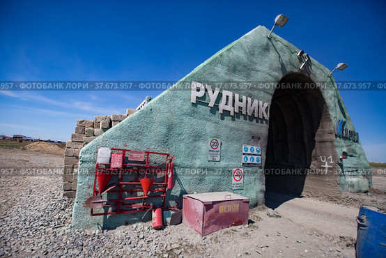 Khromtau, Aktobe region, Kazakhstan - May 06 2012: Gold ore mine portal. Title: Quarry (left) and Mechel company logo (right). Red firefighter tools and fire sand box. Blue sky and desert. Редакционное фото, фотограф Alexey Rezvykh / Фотобанк Лори