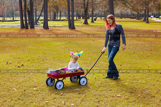 Kid girl and mother walking in the park with pull cart. Стоковое фото, агентство Ingram Publishing / Фотобанк Лори