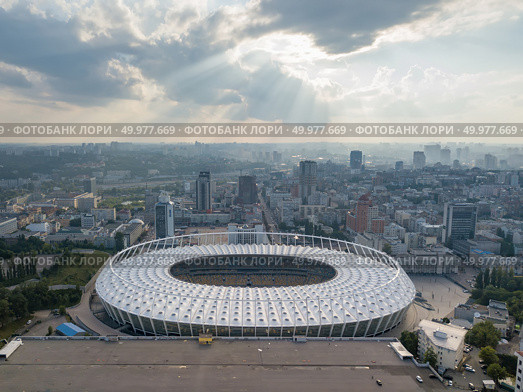 KIEV, UKRAINE - July 19, 2018. Aerial view from drone to a city landscape and National Olimpic Complex in Kiev, Ukraine at sunset on a background cloudy sky in a summer day.. KYIV, UKRAINE - July 19, 2018. National Sports Complex Olympic, stadium NSC Olimpiysky. Panoramic viev from drone of cityscape and the stadium. Редакционное фото, агентство Ingram Publishing / Фотобанк Лори