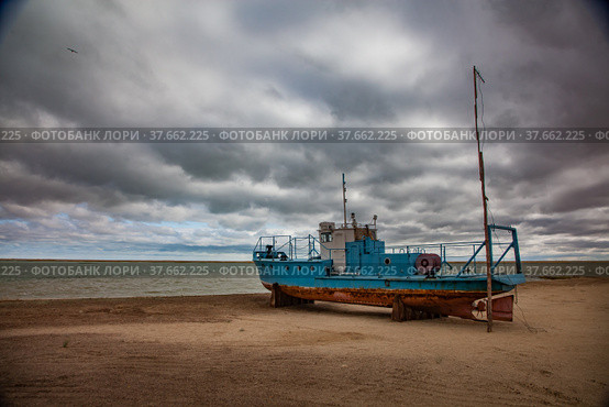 Kok-aral, Kazakhstan - 03 May, 2012: Small Aral sea Kok-aral sand dam. Fishing boat on the beach. Aral on horizon. Grey stormy clouds. Стоковое фото, фотограф Alexey Rezvykh / Фотобанк Лори