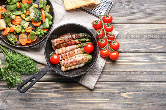 Композиция со вкусным беконом, завернутым спаржей в сковороде на деревянном столе. Стоковое фото, фотограф Pixel_shot / Фотобанк Лори