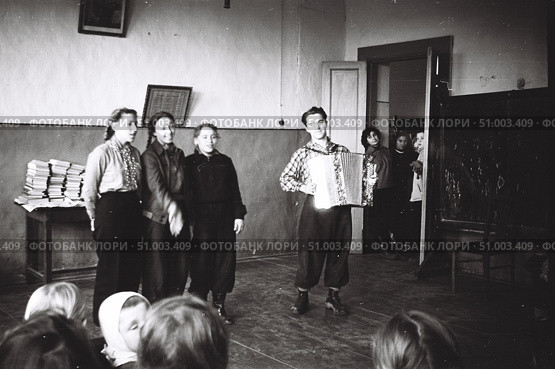 Концерт самодеятельности в деревенской школе, 1950-е годы. Три девушки поют  и молодой человек играет на баяне. Зрители заглядывают в дверь школьного класса. Стоковое фото, фотограф Retro / Фотобанк Лори