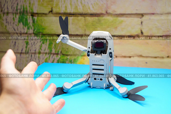 Квадрокоптер Dji Mini 2 бездельничает сидя на столе и приветствует человека поднятой лапкой с винтами, во время запрета на полеты дронов (2023 год). Редакционное фото, фотограф Sergei Gorin / Фотобанк Лори