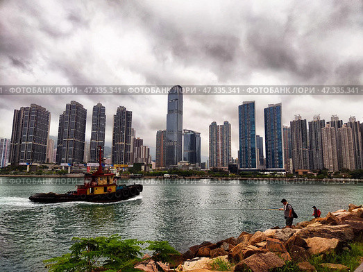 Lantau Island, Hong Kong - April 09, 2024: Fishing by the harbor with a city skyline in the background during a cloudy day in Lantau, Hong Kong. Редакционное фото, фотограф Кривошеина Елена Леонидовна / Фотобанк Лори