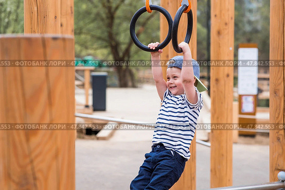 Lifestyle. A cute little boy is hanging on rings on a sports field in the fresh air. The concept of children's sports and physical development. Стоковое фото, фотограф Photojuli / Фотобанк Лори