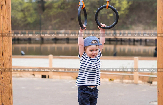 Lifestyle. A cute little boy is hanging on rings on a sports field in the fresh air. The concept of children's sports and physical development. Стоковое фото, фотограф Photojuli / Фотобанк Лори