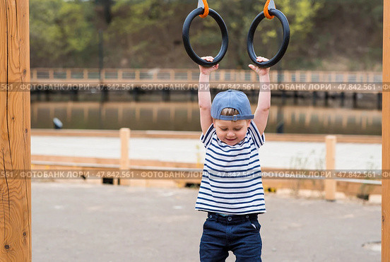 Lifestyle. A cute little boy is hanging on rings on a sports field in the fresh air. The concept of children's sports and physical development. Стоковое фото, фотограф Photojuli / Фотобанк Лори