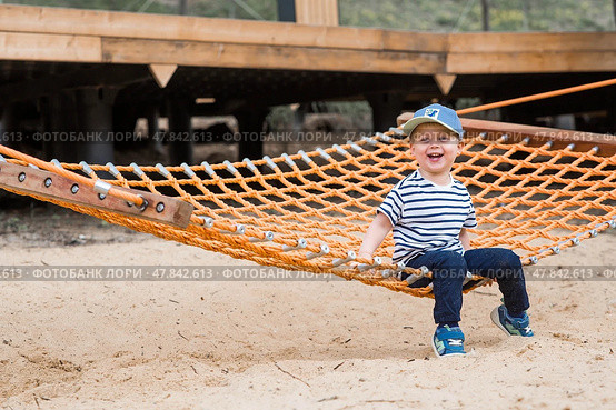 Lifestyle. A cute little boy is sitting in a hammock on a modern outdoor playground. The concept of family entertainment and leisure. Стоковое фото, фотограф Photojuli / Фотобанк Лори