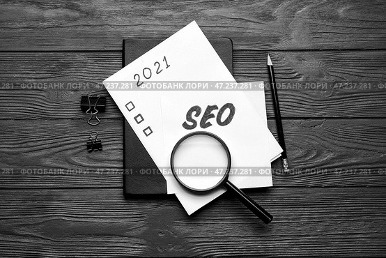 Лист бумаги с аббревиатурой SEO, списком дел, лупой и канцелярскими принадлежностями на фоне темного дерева. Стоковое фото, фотограф Pixel_shot / Фотобанк Лори