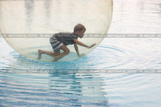 Little boy have fun inside big plastic balloon on the water of swimming pool on the summer resort. Kid inside big inflatable transparent ball running and having fun. Стоковое фото, фотограф Nataliia Zhekova / Фотобанк Лори