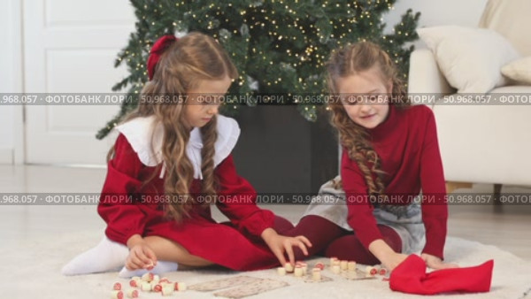Little children girls play russian lotto board game at home on the Christmas tree background. Children early development. Christmas and New Year holidays time. Board game and kids leisure concept. Footage. Стоковое видео, видеограф Ирина Михайличенко / Фотобанк Лори