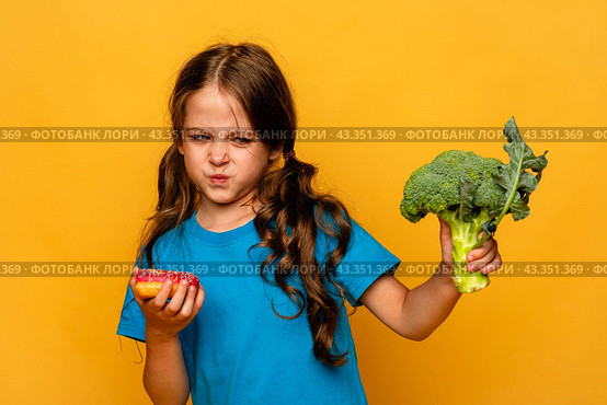 Little cute kid girl refusing to eat healthy vegetables broccoli on yellow background. Children do not like to eat vegetables. Стоковое фото, фотограф Ирина Михайличенко / Фотобанк Лори