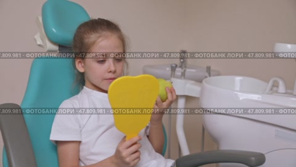 Little girl are eating green apple in the dentist's chair and looking in the mirror at her teeth. Healthy teeth concept. Child eat a green apple. Slow motion footage. Стоковое видео, видеограф Ирина Михайличенко / Фотобанк Лори