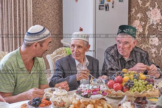 Local residents of Siberian village celebrate Muslim holiday Kurban Bayram at their home table. Mullah talking with villagers. Eid al-Adha (2021 год). Редакционное фото, фотограф Ирина Кононова / Фотобанк Лори