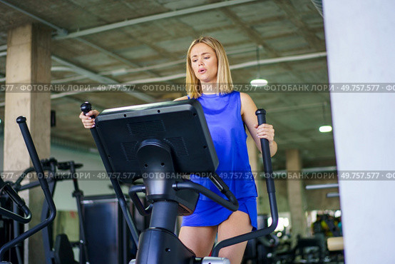Low angle view horizontal photo with copy space of a blonde young caucasian woman walking exercising in elliptical machine in the gym. Woman walking exercising in elliptical machine in the gym. Стоковое фото, агентство Ingram Publishing / Фотобанк Лори