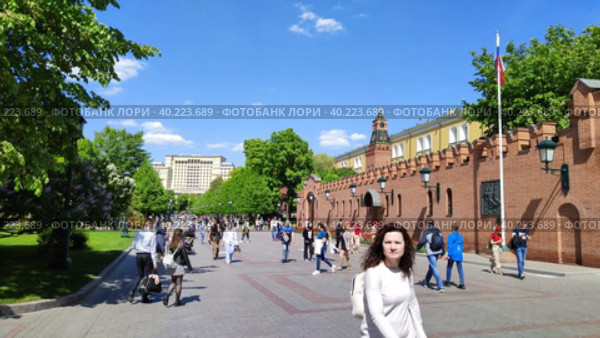 Люди гуляют по Александровскому саду возле Московского Кремля. Популярный туристический маршрут. Флаг Российской Федерации на флагштоке. Жители и гости столицы прогуливаются. Москва, Россия - 30 мая 2022. People walk in the Alexander Garden near the Moscow Kremlin. A popular tourist route. The flag of the Russian Federation on the flagpole. Residents and guests of the capital are walking. Moscow, Russia - May 30, 2022. Редакционное видео, видеограф Ирина / Фотобанк Лори