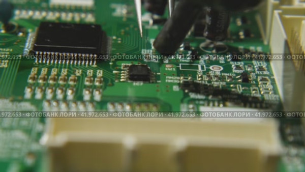 Macro video of a repairman using tweezers and a soldering station to remove a chip from an electronic board. Underneath the microchip is boiling brazing flux. Electronics, computer, TV repair shop. Стоковое видео, видеограф Воловодов Владимир / Фотобанк Лори