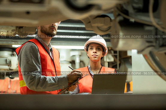 Male and female engineers work together in an electric repair station. Inspecting the undercarriage of electric train that are being repaired at the garage. Стоковое фото, агентство Ingram Publishing / Фотобанк Лори