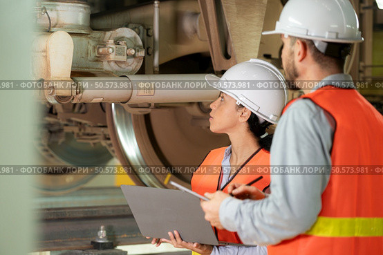 Male and female engineers work together in an electric repair station. Inspecting the undercarriage of electric train that are being repaired at the garage. Стоковое фото, агентство Ingram Publishing / Фотобанк Лори