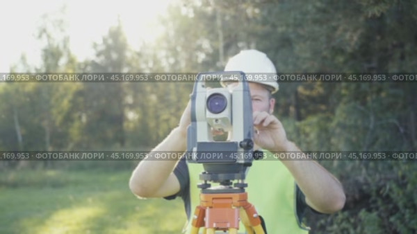 Male engineer surveyor near a surveying instrument preparing to start taking precise measurements. Geodetic work, topography, land surveying, cadastral work. Стоковое видео, видеограф Скрипачев Антон / Фотобанк Лори