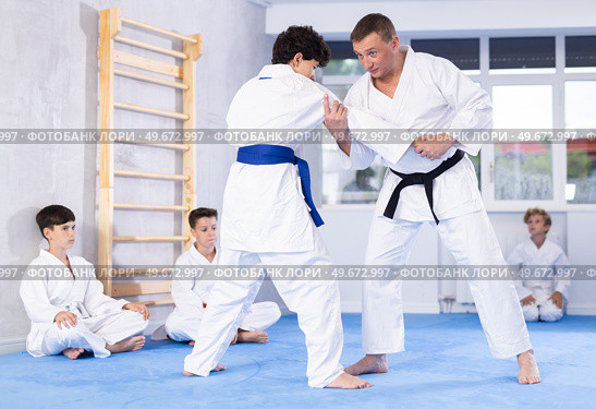 Male karate instructor training little child wearing kimono in dojo or jiu-jitsu in gym. Стоковое фото, фотограф Яков Филимонов / Фотобанк Лори