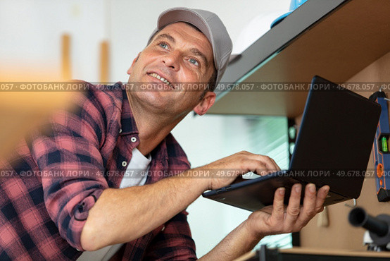 male worker assembles new white furniture reading instruction on laptop. Стоковое фото, агентство Ingram Publishing / Фотобанк Лори