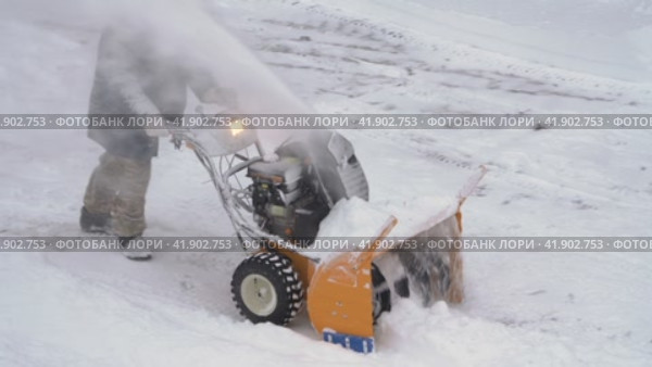 Male worker is using snowblower to remove snow after winter cyclone. Worker is blowing snow after blizzard (2023 год). Редакционное видео, видеограф А. А. Пирагис / Фотобанк Лори